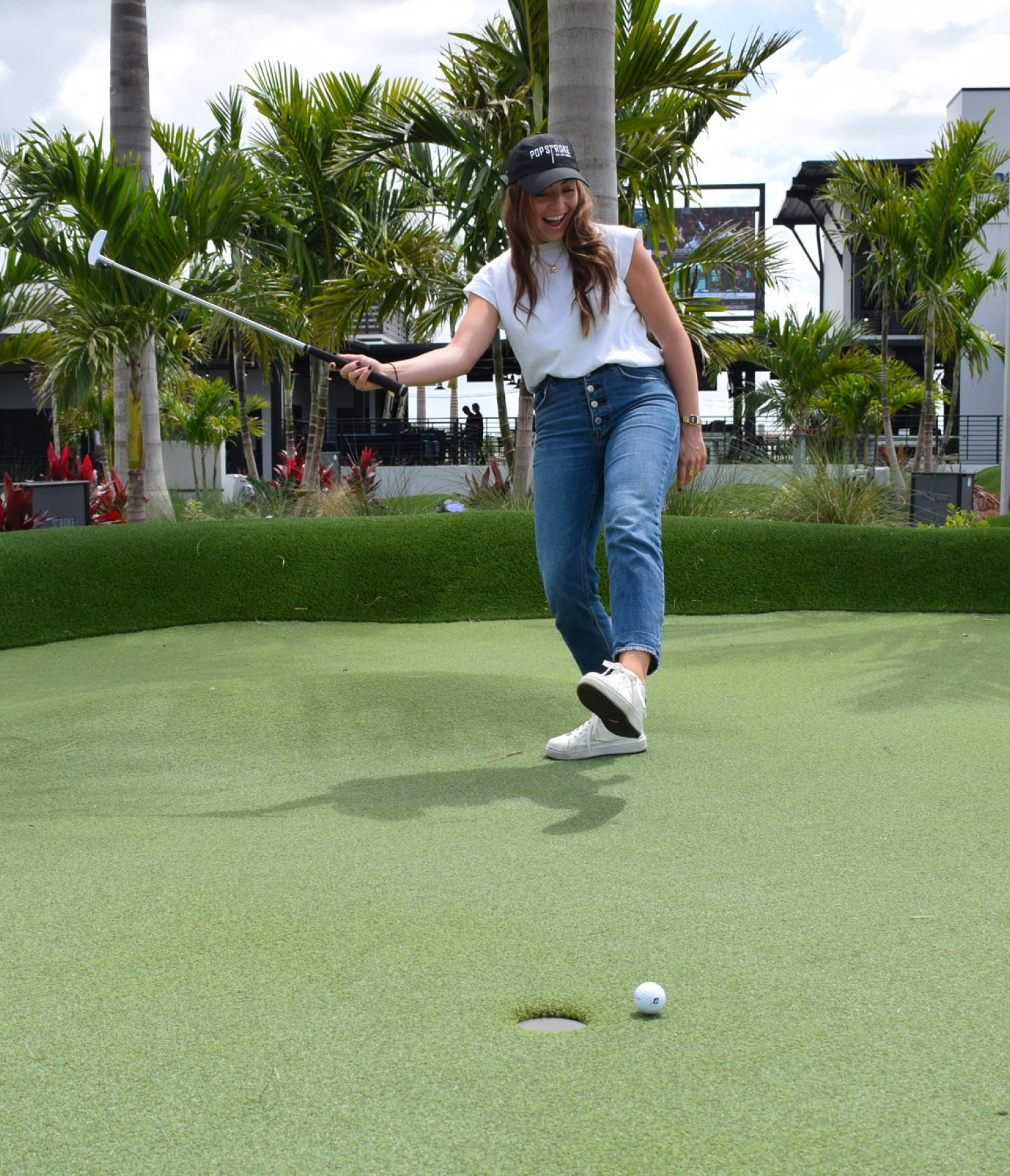 A woman standing on a golf course, holding a golf club after taking a swing.